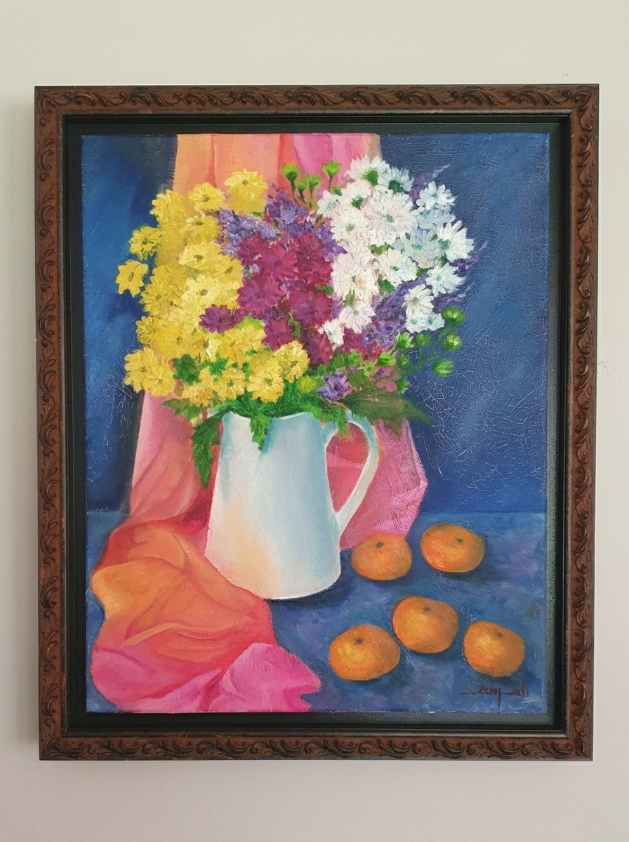 Daisies in a white pitcher beside fruit and draped fabric